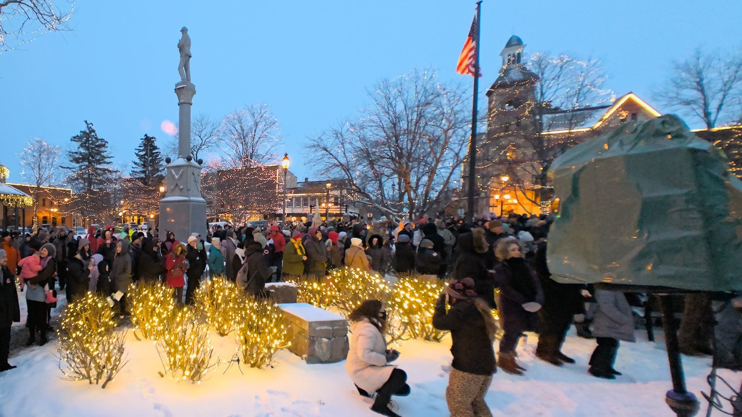Christmas lights glowing against fallen snow with people gathering for groundhog day.