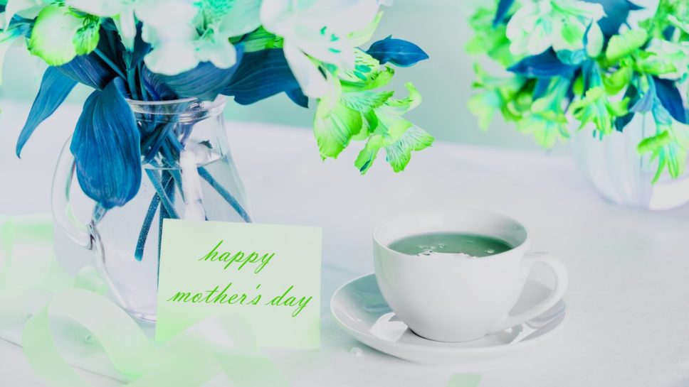 Beautiful bouquet of alstroemeria in a vase with water, white cup of tea, greeting card with the inscription happy mother's day.