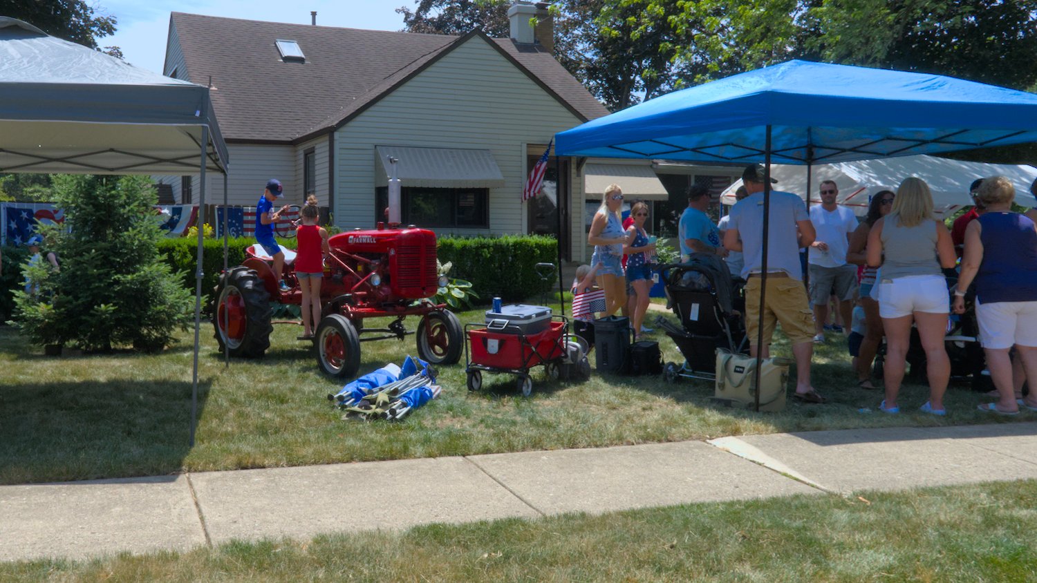 Farmall tractor parked in yard next to canopy of parade goers.