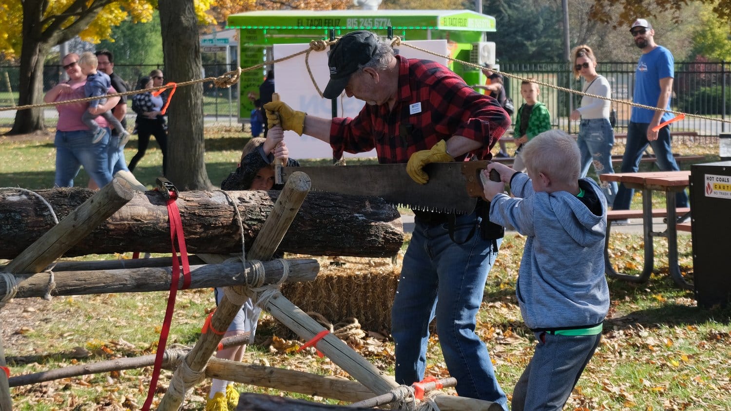 Two boys getting helped with a double buck saw.