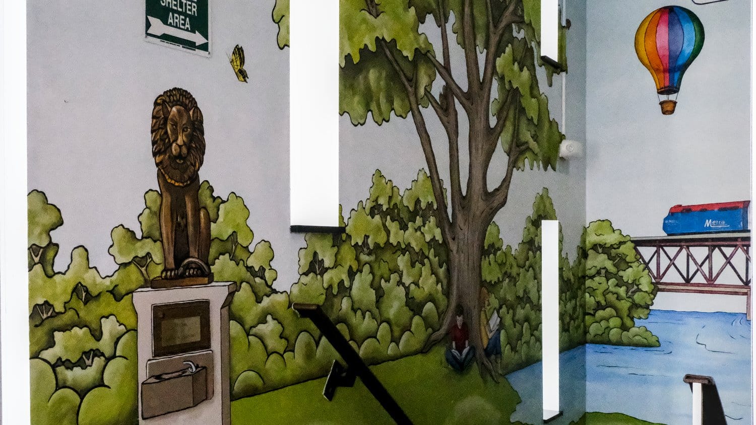 Summer stairwell mural featuring the Lion's Park lion statue and the Metra.