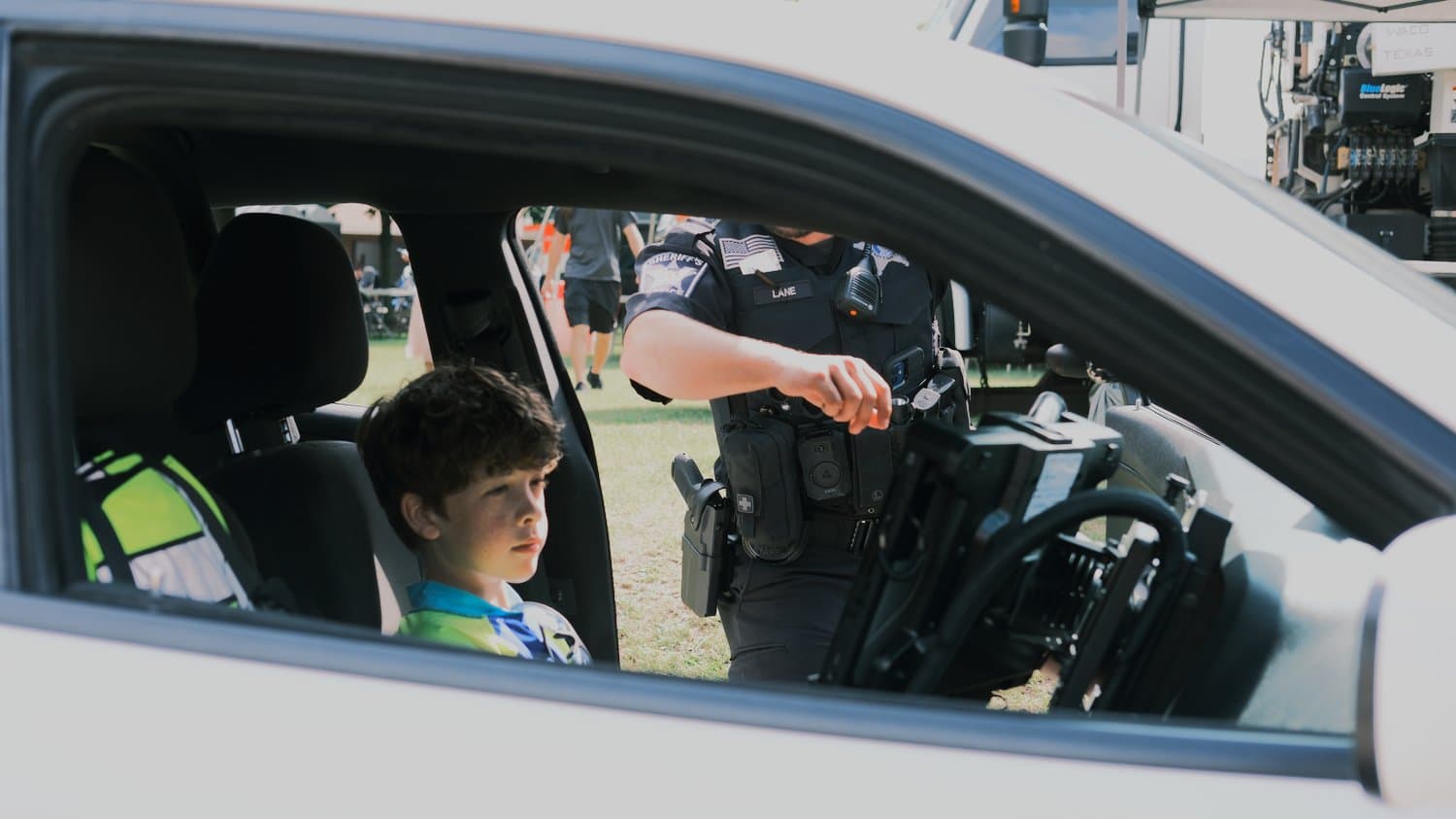 Boy in sheriff's car as sheriff points out controls.