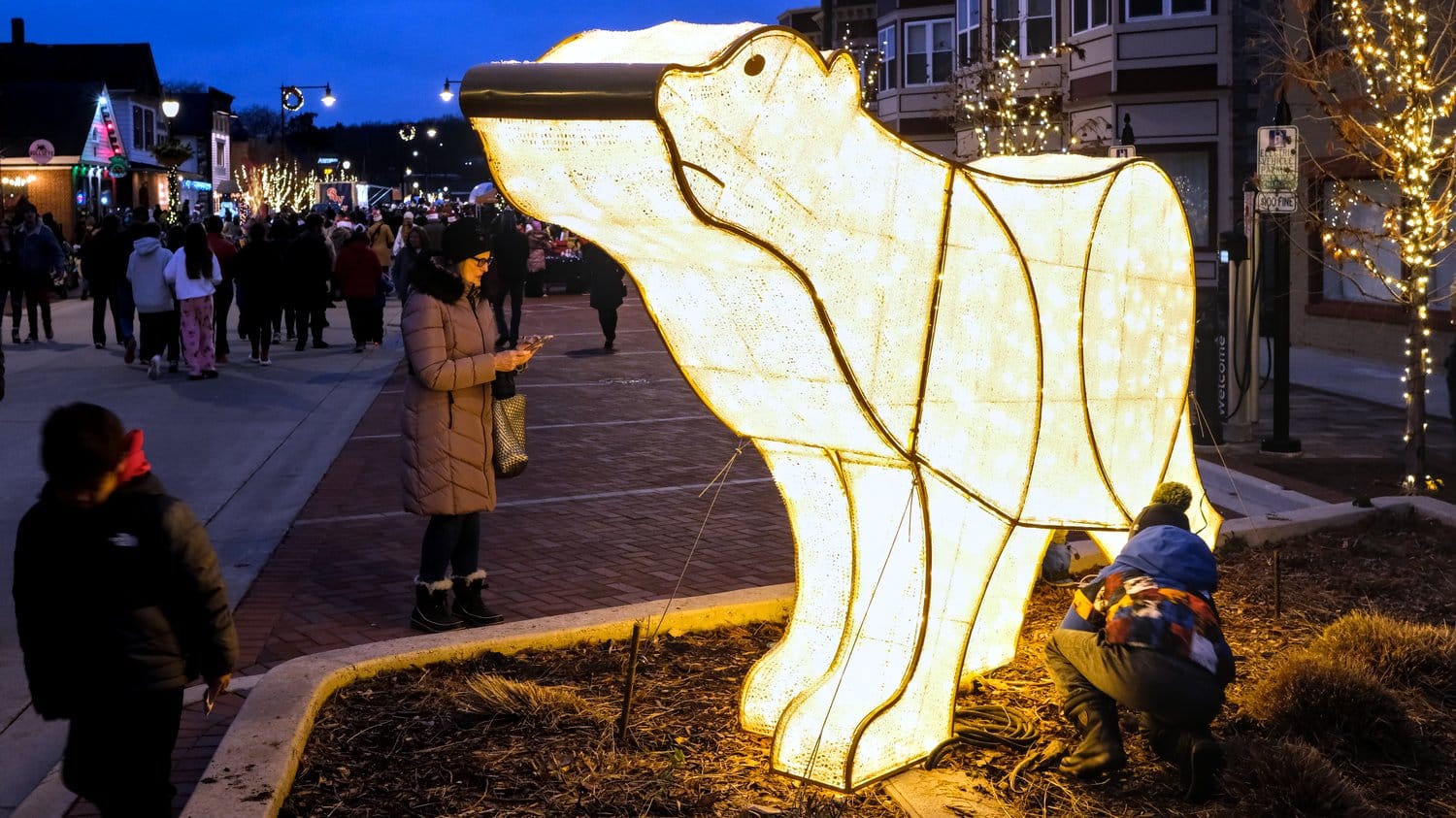 Children playing around lighted polar bear decoration.