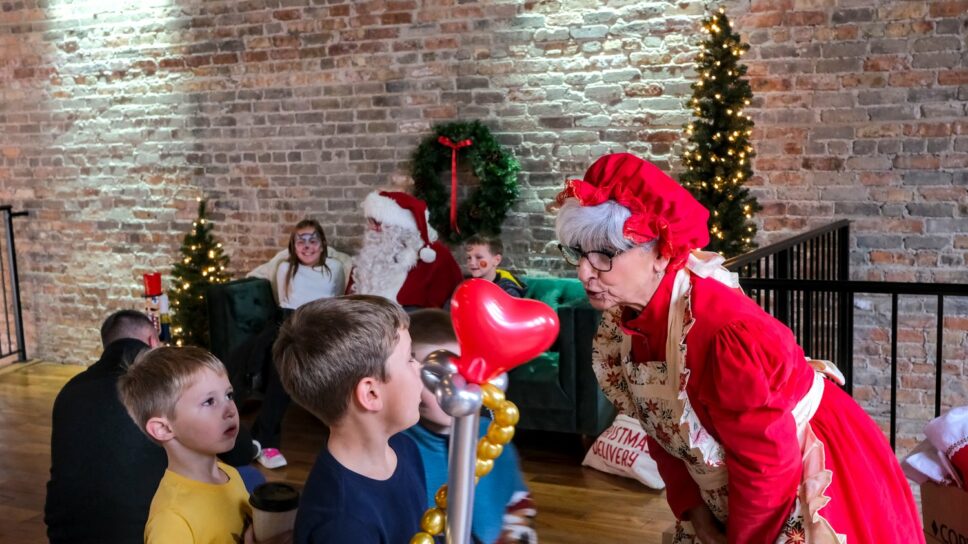 Mrs. Claus talking to children while Santa poses for pictures.