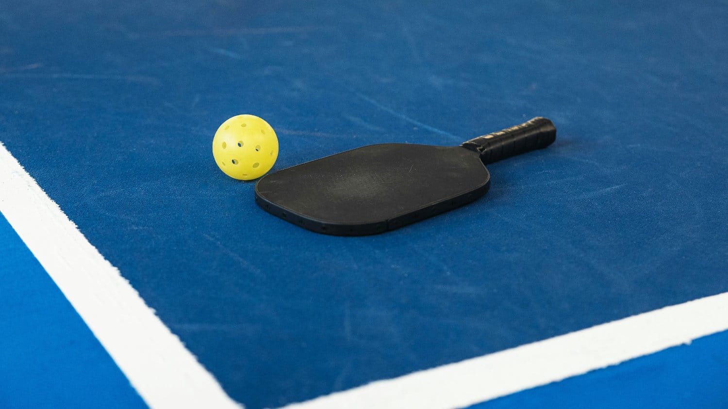 Pickleball paddle and ball laying on the pickleball court.
