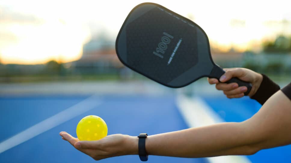 Person holding pickleball paddle and ball.